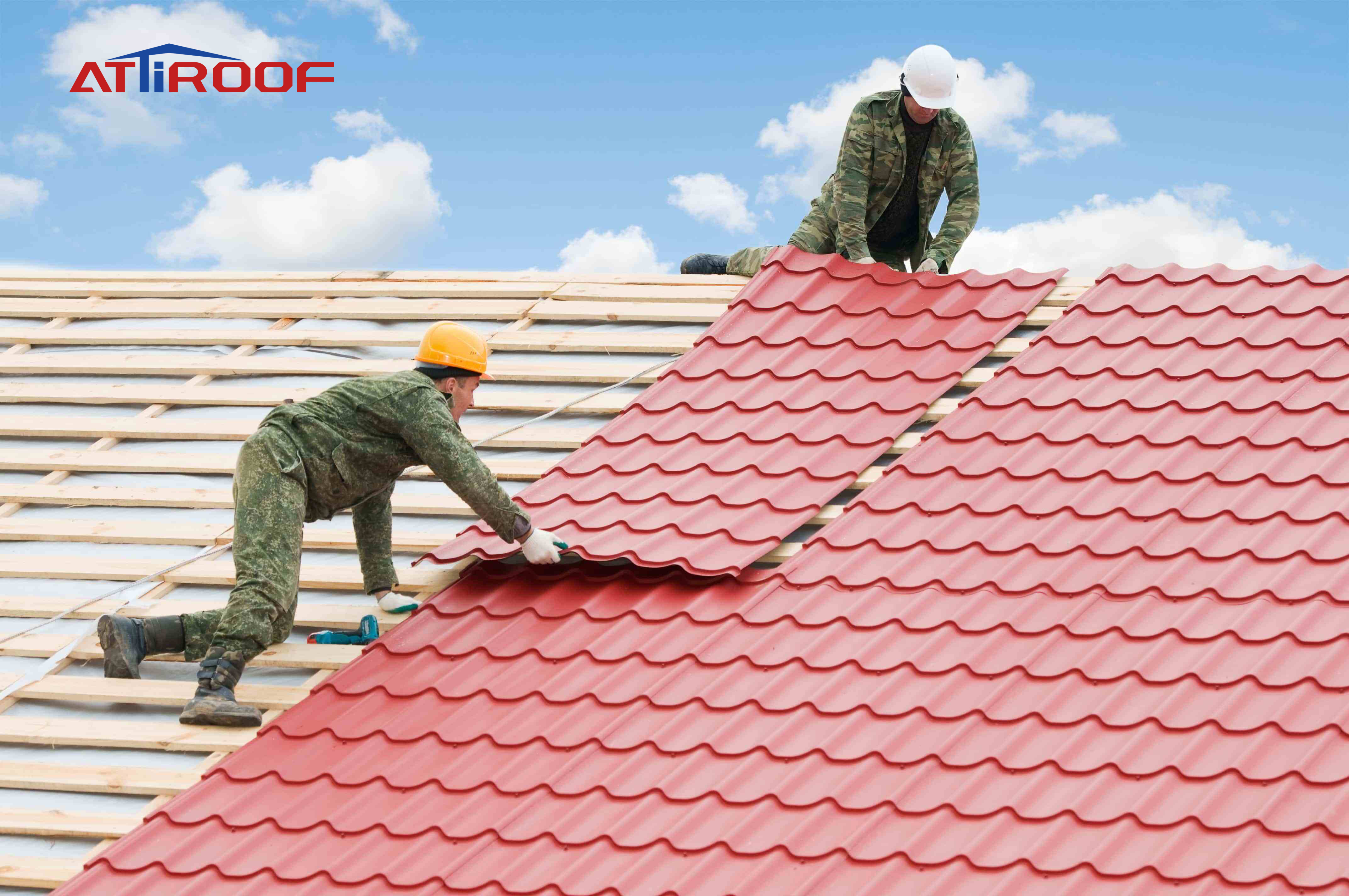Roofers in safety gear professionally installing red synthetic resin tiles on a new roof under a clear sky.